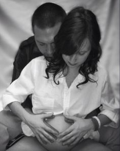 a pregnant woman sitting next to a man holding her belly and looking down at her stomach