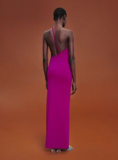 the back of a woman in a pink dress standing against an orange background with her hands on her hips