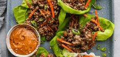 lettuce wraps filled with meat and carrots on a blue plate next to dipping sauce