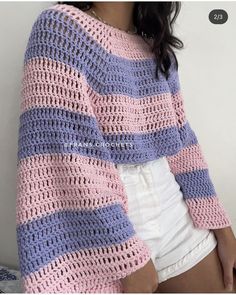 a woman wearing a pink and blue crocheted sweater with stripes on the sleeves