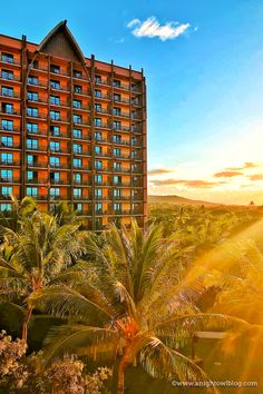 the hotel is surrounded by palm trees in front of a blue sky with clouds and sun beams