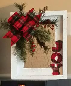 a red and black plaid bow on top of a white frame with pine branches in it