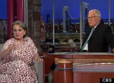 an older woman sitting next to a man on a tv set in front of a window