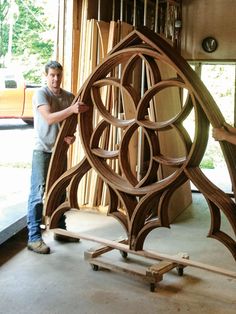 a man standing next to a large wooden object in a room with lots of windows