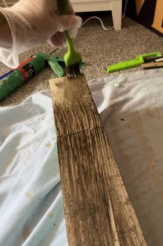 a person is using a green tool to paint a piece of wood on the floor