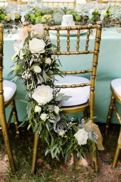 an arrangement of flowers and greenery on the back of chairs