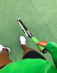 a person holding a tennis racquet on top of a green court with white shoes