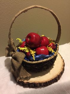 a basket filled with red apples sitting on top of a wooden slice next to a white table cloth