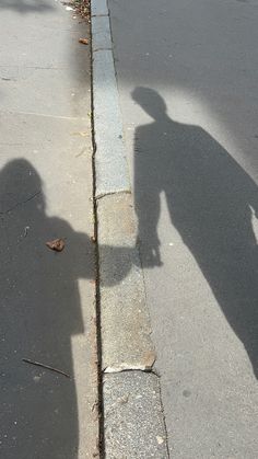 the shadow of a person riding a skateboard on a city street next to a curb