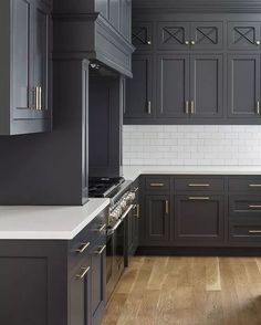 a kitchen with dark gray cabinets and white counter tops, gold pulls on the handles