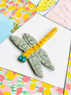 a dragonfly brooch sitting on top of a piece of paper next to scissors