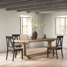 a wooden table with four chairs and a vase on it in a white walled room