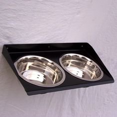 two stainless steel bowls sit in the middle of a black tray on a white background