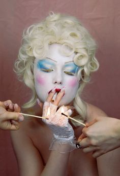 a woman with makeup on her face and hands holding sticks in front of her face