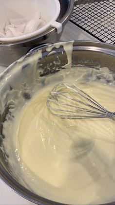 a metal bowl filled with batter and whisk on top of a table next to other bowls