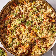 a pan filled with rice and vegetables on top of a white counter next to a spoon