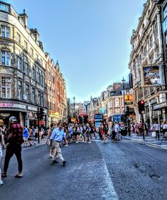 many people are crossing the street in front of some buildings on a busy city street