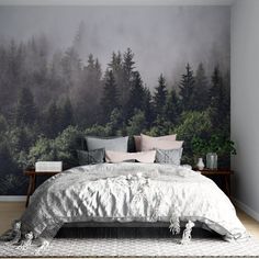 a bed with pillows and blankets in front of a forest mural on the wall behind it