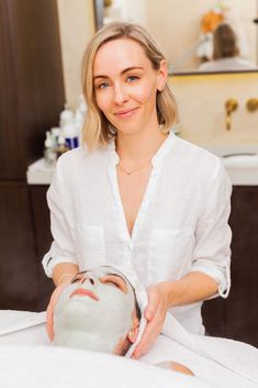 a woman in a white shirt is getting a facial mask on her face and smiling at the camera