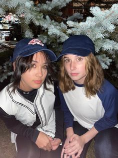 two women sitting next to each other in front of a blue tree with snow on it