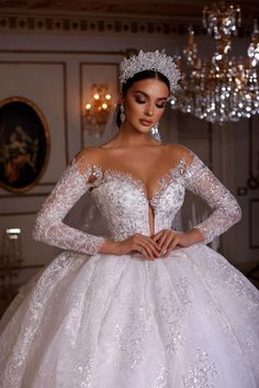 a woman in a white wedding dress standing next to a chandelier and wearing a tiara