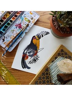 a bird painted on paper next to some paintbrushes and other art supplies in front of it