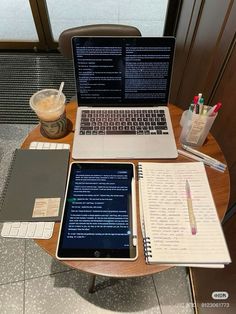 an open laptop computer sitting on top of a wooden table next to a notebook and pen