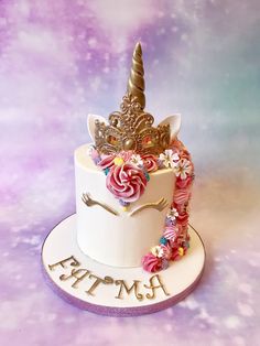 a white cake decorated with pink flowers and a gold unicorn horn topper on a purple background