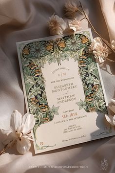 a wedding card with flowers and leaves on top of white fabric, surrounded by silk