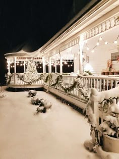 a white house covered in snow with christmas lights on the front porch and trees around it