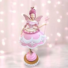 a pink fairy figurine sitting on top of a cake