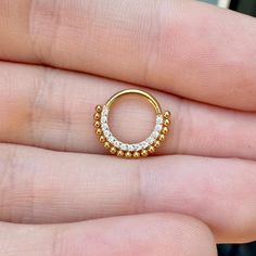 a person is holding an open gold ring with small white stones on the inside of it