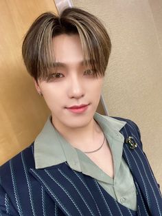 a young man wearing a blue shirt and silver necklace posing for a photo in front of a wooden wall