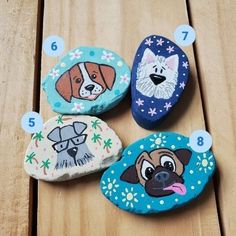 four painted rocks with dogs on them sitting on a wooden table next to each other