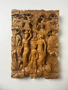 an intricately carved wooden wall panel with two people holding a vase and tree branches