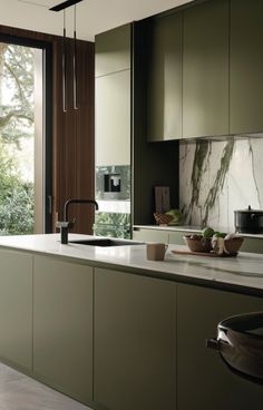 a kitchen with green cabinets and marble counter tops, along with a large window that looks out onto the trees outside