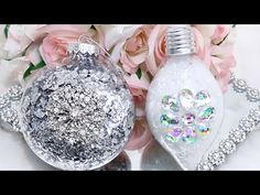 two silver and white ornaments sitting on top of a table next to pink flowers in vases