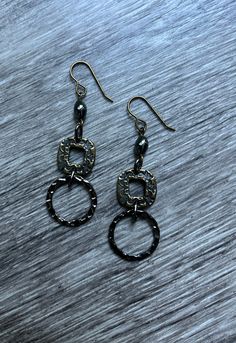 Mixed metal patterned bronze and hammered gunmetal dangle earrings.  A round hammered gunmetal loop, a patterned bronze link and an oval hematite bead  are combined to form these geometric earrings.  The patterned bronze link has a different pattern on each side.  The drop length is 2 1/8 inches.  Bronze ear wires. Nickel-free Pewter Jewelry In Gunmetal, Metal Earrings With Oxidized Finish, Gunmetal Dangle Earrings Metal Jewelry, Bronze Dangle Metal Earrings, Gunmetal Dangle Jewelry, Gunmetal Metal Earrings Gift, Gunmetal Dangle Earrings, Gunmetal Metal Earrings For Gift, Antique Gold Metal Earrings With Antique Finish