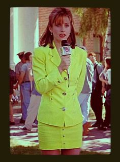 a woman in a yellow suit is holding a microphone and talking to someone on the sidewalk