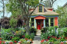 a colorful house with flowers in the front yard and trees on either side of it