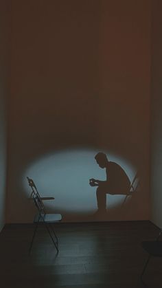 a man sitting in a chair next to a wall with a shadow projected on it