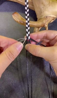 two hands are working on an object with black and white striped yarn, while another hand is holding the string