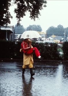 two people walking in the rain with an umbrella over their heads and one holding a child