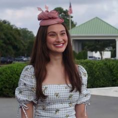 a woman with long hair wearing a dress and hat smiling at the camera while standing in front of a building