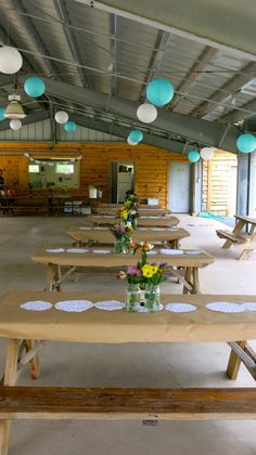 tables and benches are lined up in an empty room with paper lanterns hanging from the ceiling