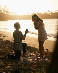 a man kneeling down next to a woman on a beach