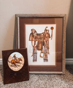 two framed pictures sitting on top of a carpeted floor next to a wall mounted painting