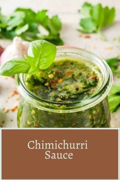 a glass jar filled with green sauce next to basil leaves