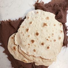 three tortillas on a brown cloth and some other food items in the background