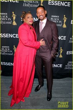 a man and woman standing next to each other in front of a red carpeted wall